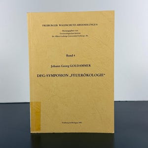 May include: A softcover book with a textured light yellow cover. The text reads: FREIBURGER WALDSCHUTZ-ABHANDLUNGEN, Herausgegeben vom Forstzoologischen Institut der Albert-Ludwigs-Universität Freiburg i. Br., Band 4, Johann Georg GOLDAMMER, DFG-SYMPOSION FEUERÖKOLOGIE, Freiburg im Breisgau 1983.
