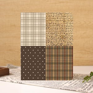 May include: A rectangular notebook cover featuring a four-quadrant design. The top left is a beige and white plaid, the top right is tan with black cursive script, the bottom left is dark brown with white hearts, and the bottom right is a brown plaid.