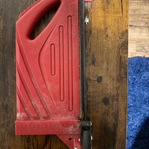 May include: A red Roberts brand flooring cutter tool. The tool has a red handle and a black blade. The tool is on a brown wooden surface.