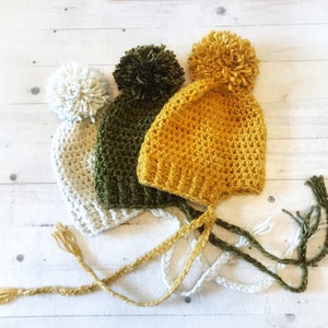 May include: Three crocheted hats with pom-poms in white, green, and yellow.