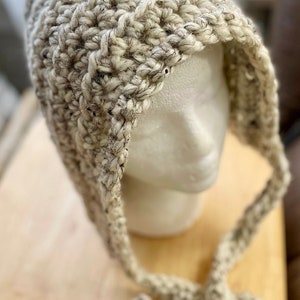 May include: A white crocheted hat with a long, dangling tie. The hat has a textured, chunky knit and is accented with black flecks.