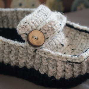May include: A crocheted slipper with a beige and black color scheme. The slipper has a wooden button on the top.