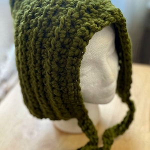 May include: A green crocheted hooded hat with a long tie. The hat is made with a thick yarn and has a simple design.