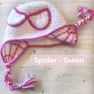 May include: White crocheted hat with a pink spider web design and a pink and white braided tassel. The hat has a pink heart-shaped patch on the front with the text "Spider - Gwen".