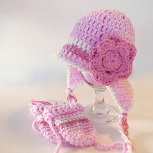 May include: A pink crocheted hat with a white trim and a pink flower. The hat has a long pink and white crocheted tie. A matching pair of pink and white crocheted mittens are included.