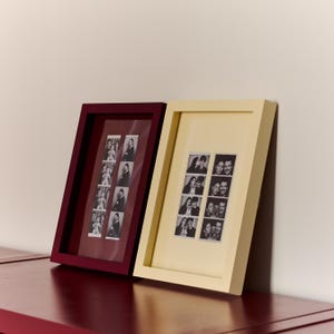 Peut inclure: Deux cadres photo rectangulaires, l'un bordeaux foncé et l'autre crème, contenant chacun une bande verticale de photos en noir et blanc. Les cadres sont placés côte à côte et présentent plusieurs petits portraits de personnes.