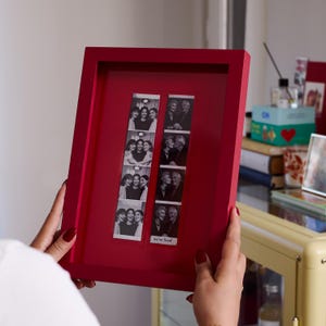 Red custom photobooth strip frame held by hand, highlighting the personalized photo opening, layered mat design, and handmade construction. Designed to showcase wedding photo booth strips and special memories in a stylish modern picture frame. Unique personalized gift and contemporary wall decor for newlyweds, couples, friends, and family, suitable for weddings, anniversaries, Valentine's Day, Christmas, birthdays, and other meaningful celebrations.