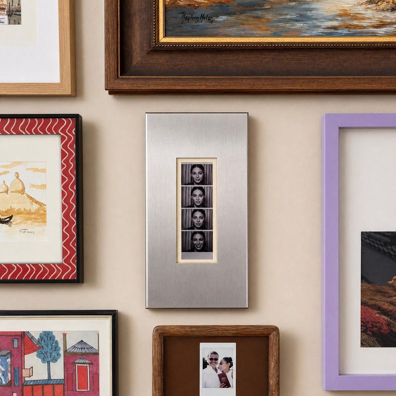 May include: A silver metal photo frame with four black and white photo booth style images of a woman. The frame is rectangular and mounted on a beige wall, surrounded by other framed artwork.