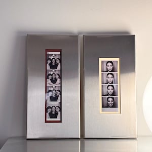May include: Two rectangular, brushed metal photo frames. Each frame holds a series of black and white photo booth style images. One frame has a red border, the other a cream border. The photos feature groups of women.