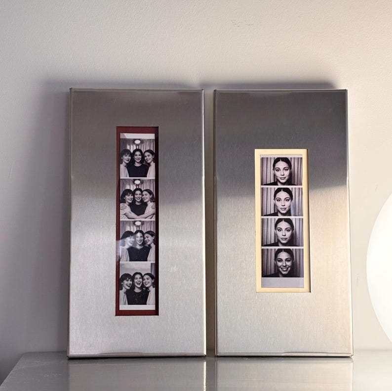 May include: Two rectangular, brushed metal photo frames. Each frame holds a series of black and white photo booth style images. One frame has a red border, the other a cream border. The photos feature groups of women.