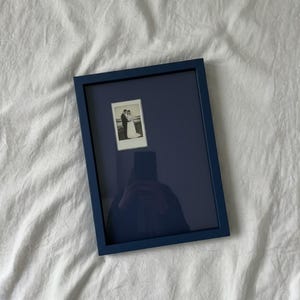 May include: A navy blue framed photograph featuring a black and white image of a couple. The frame has a simple, rectangular design. The photograph is displayed on a white surface.