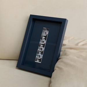 Navy blue personalized photobooth strip frame featuring a vertical black and white photo strip, styled as modern minimalist wall decor. Custom 9x13 inch picture frame designed for wedding photo booth memories, engagement photos, anniversary pictures, and meaningful keepsakes. Stylish personalized gift for couples, newlyweds, husbands, wives, friends, and family, perfect for weddings, anniversaries, Christmas, birthdays, Valentine's Day, and gallery wall displays.