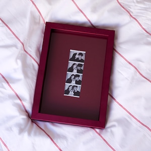 Red personalized photobooth strip frame displaying a vertical wedding photo booth strip, combining bold color with a modern minimalist picture frame design. Custom photo frame perfect for preserving wedding memories, engagement photos, anniversary moments, and special event photographs. A unique personalized wedding gift, anniversary gift, Valentine's Day gift, Christmas present, birthday gift, or romantic photo keepsake for couples.