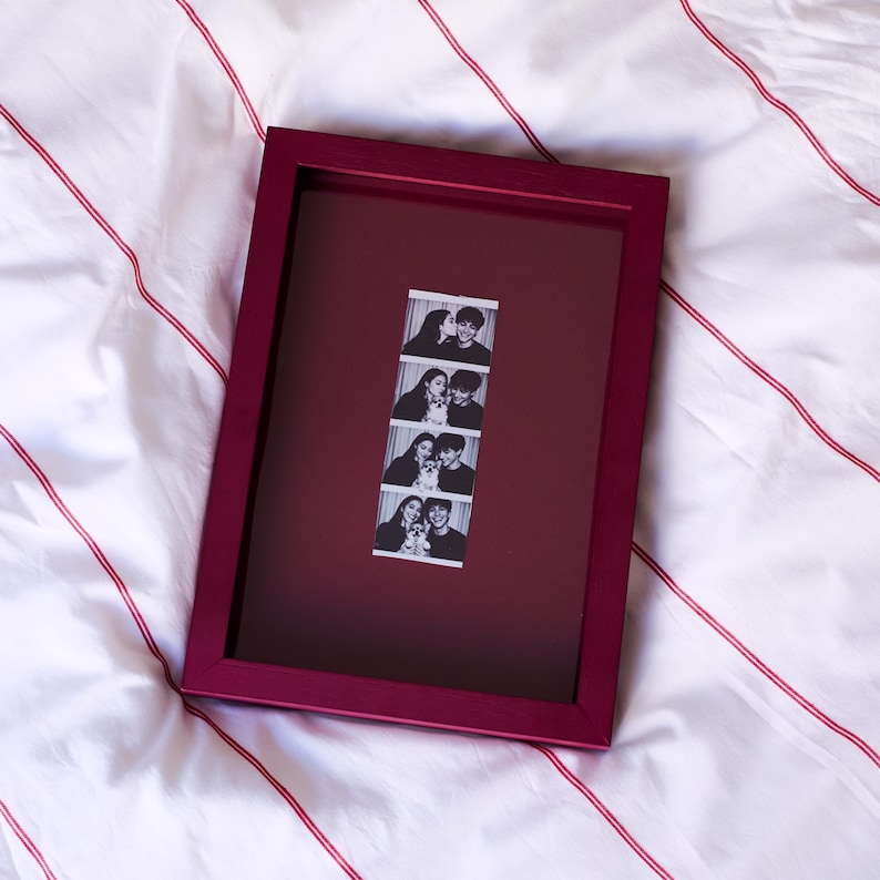 Red personalized photobooth strip frame displaying a vertical wedding photo booth strip, combining bold color with a modern minimalist picture frame design. Custom photo frame perfect for preserving wedding memories, engagement photos, anniversary moments, and special event photographs. A unique personalized wedding gift, anniversary gift, Valentine's Day gift, Christmas present, birthday gift, or romantic photo keepsake for couples.