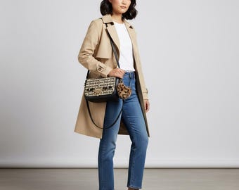 May include: A woman wearing a tan trench coat, white t-shirt, and blue jeans, carrying a black and white crossbody bag with the words "Juicy Couture" printed on it. A small leopard print charm hangs from the bag. Black loafers complete the outfit.