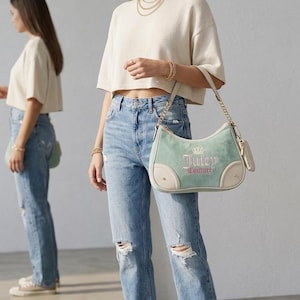 May include: A light green velour shoulder bag with cream-colored leather trim, featuring the embroidered text Juicy Couture and a crown logo in pink and gold. The bag includes a gold chain strap and a small matching pouch attached to the side.