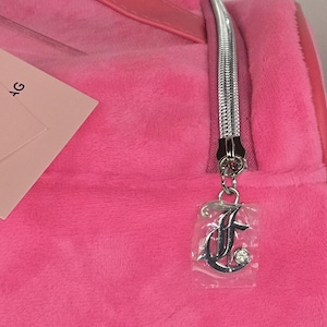 Close-up of a silver zipper pull shaped like the letter J with a rhinestone accent on the pink bag.