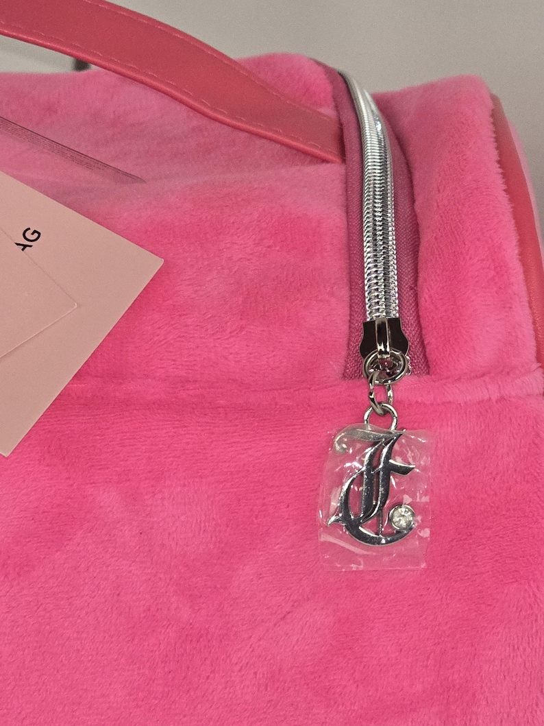 Close-up of a silver zipper pull shaped like the letter J with a rhinestone accent on the pink bag.