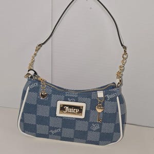 May include: Blue denim shoulder bag with a chequered pattern and white trim. It has gold-tone chain straps and a rectangular gold plaque with the word "Juicy". Charms include a heart and a key.