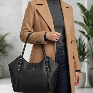 May include: A black pebbled leather tote bag featuring two thin shoulder straps, silver-toned hardware, and buckle accents on the sides. The front of the bag displays the London Fog logo in silver text centered near the top opening.
