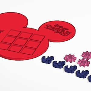 Puede incluir: Una bandeja roja con forma de Mickey Mouse con nueve recortes cuadrados y el texto "Disney Destiny". Varias piezas de plástico azules y rosas están dispersas cerca. La imagen es una representación 3D.