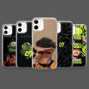 May include: A collection of five iPhone cases featuring images of a race car driver. The cases display the driver's portrait, helmet, and the name "Lando Norris" in various designs, including hearts and abstract patterns. The cases are in black, orange, and green.