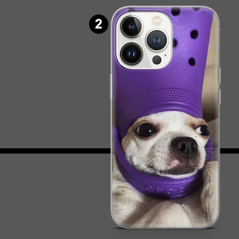 May include: A phone case featuring a white and tan Chihuahua wearing a purple clog on its head. The case has a clear background and a close-up of the dog's face. The phone's camera lenses are visible at the top.