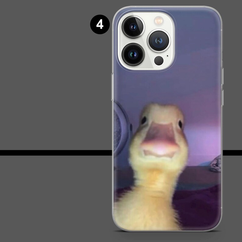 May include: A clear phone case featuring a close-up image of a yellow duckling with a pink beak. The phone case has a purple background and a camera module at the top.