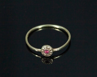 May include: A delicate gold ring with a small, round red gemstone set in a circle of tiny gold beads.