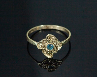 May include: A gold ring with a blue gemstone set in a swirling, ornate design.