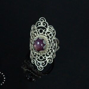 May include: A silver ring with a delicate filigree design and a purple gemstone in the center.