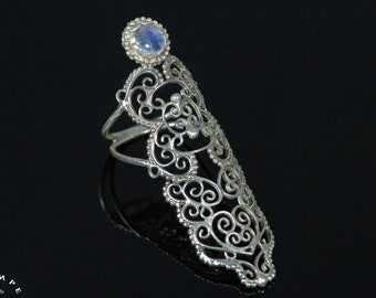 May include: A silver filigree ring with a large, round, blue moonstone. The ring is designed to be worn on the middle finger and has a delicate, intricate design.