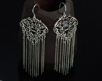 May include: Silver filigree earrings with a dangling chain design. The earrings feature a small, round, clear stone in the center of the filigree.