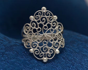 May include: A silver filigree ring with a delicate, intricate design. The ring is made of thin, twisted wires that form a pattern of swirls and loops.