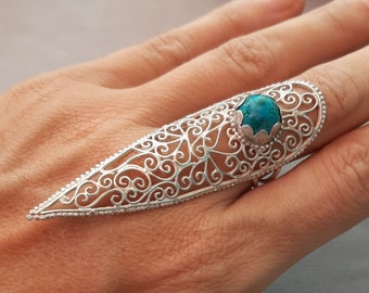 May include: A silver filigree ring with a turquoise gemstone. The ring is designed in a pointed, elongated shape and is worn on the index finger.