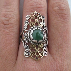 Peut inclure: Une bague en argent et or avec une pierre précieuse verte sertie dans un motif de filigrane.