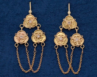 May include: A pair of gold earrings with intricate designs and small diamonds. Each earring has three tiers of dangling chains.