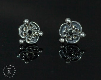 May include: A pair of silver earrings with a black stone in the center of each earring. The earrings are in the shape of a flower with intricate details.