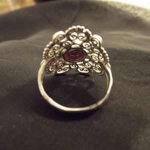 May include: A silver filigree ring with a red gemstone in the center.