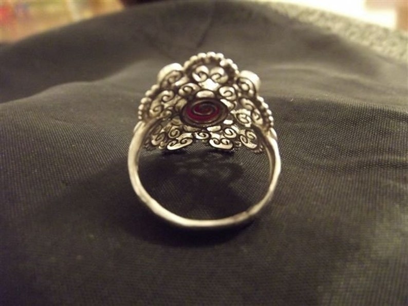 May include: A silver filigree ring with a red gemstone in the center.
