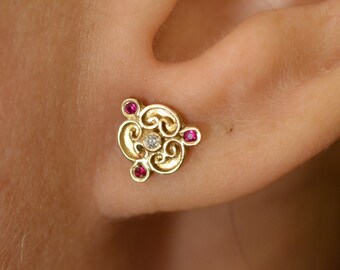 May include: Gold earring with a detailed design featuring a central diamond and four ruby accents.