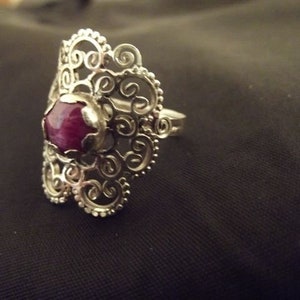 May include: A silver filigree ring with a large, round, dark pink gemstone.