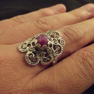 May include: A silver filigree ring with a pink gemstone set in the center.
