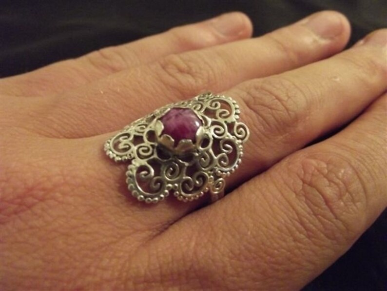May include: A silver filigree ring with a pink gemstone set in the center.