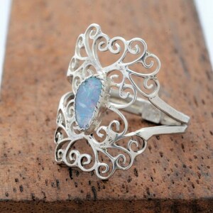 May include: A silver filigree ring with a light blue opal gemstone. The ring is designed with intricate swirls and curves.