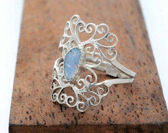 May include: A silver filigree ring with a light blue opal gemstone. The ring is designed with intricate swirls and curves.