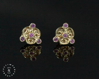 May include: A pair of gold earrings with a delicate floral design and five small purple gemstones.