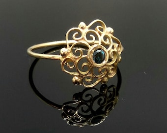May include: A gold ring with a delicate filigree design and a small blue gemstone in the center.