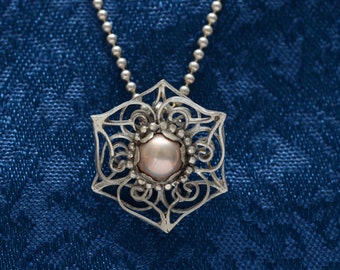 May include: A silver pendant necklace with a delicate, intricate design featuring a large, round, pink pearl in the center.