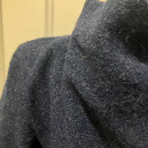 Puede incluir: Primer plano de un su&eacute;ter azul marino con cuello de cisne. El su&eacute;ter tiene una apariencia texturizada y afelpada. La tela es de color azul oscuro liso.
